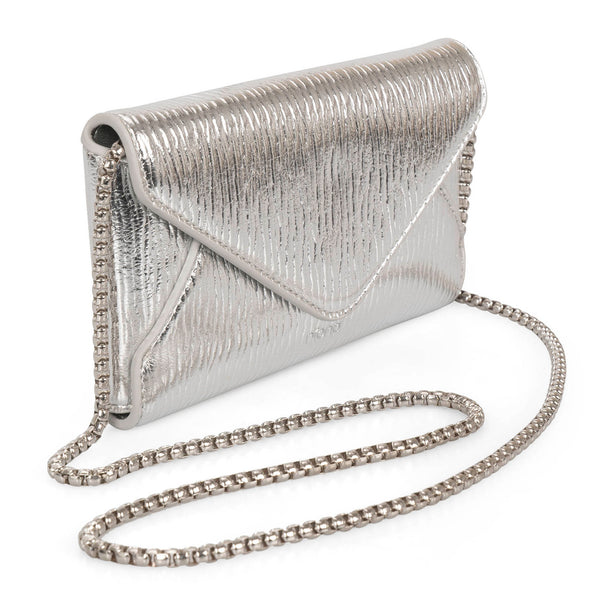Angle view of silver metallic crossbody bag called Evening in an envelopy style designed by Riona, showcasing its chain strap and shiney textured PU look.